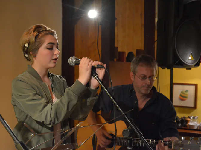 Femme qui chante devant un micro et guitariste au second plan