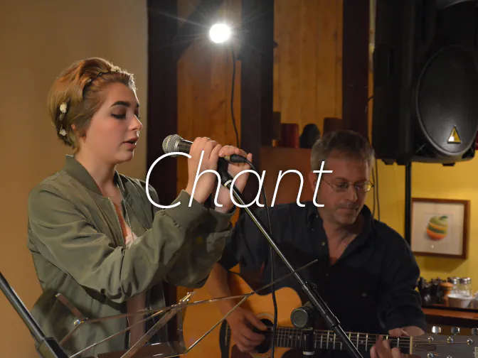 Femme qui chante devant un micro avec un guitariste au second plan